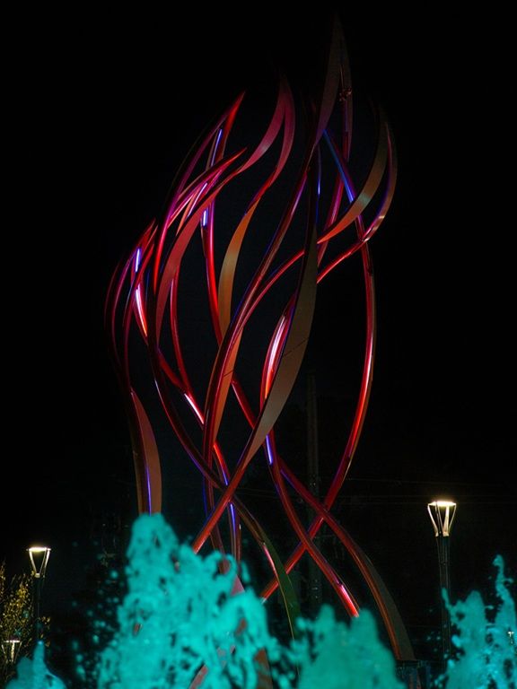 Night time image with lights and fountain of curved steel sculpture "Be the Light" by Curtis Pittman